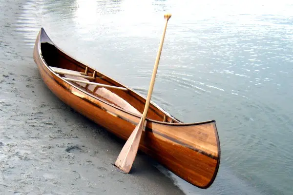 ambachtelijk gebouwde houten kano aan strand met peddel